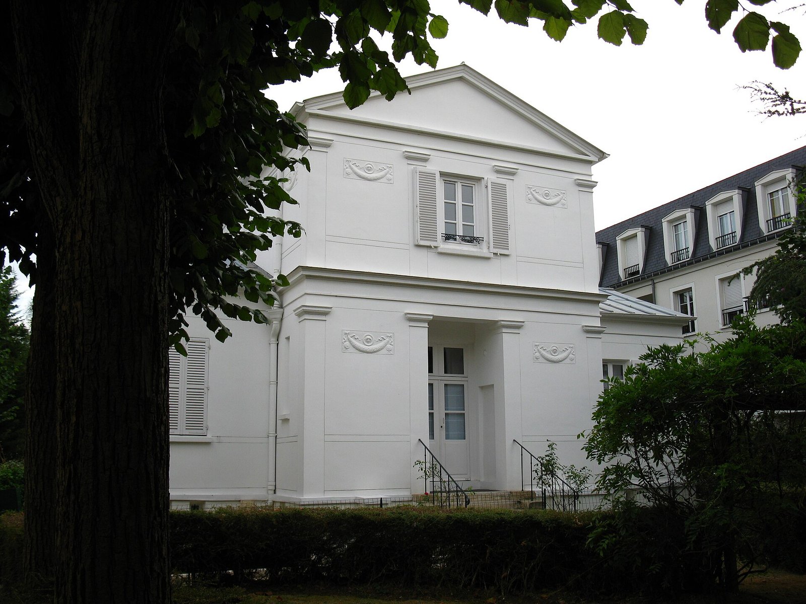 Pavillon de style Empire aux murs blancs dans un jardin arboré de Thiais